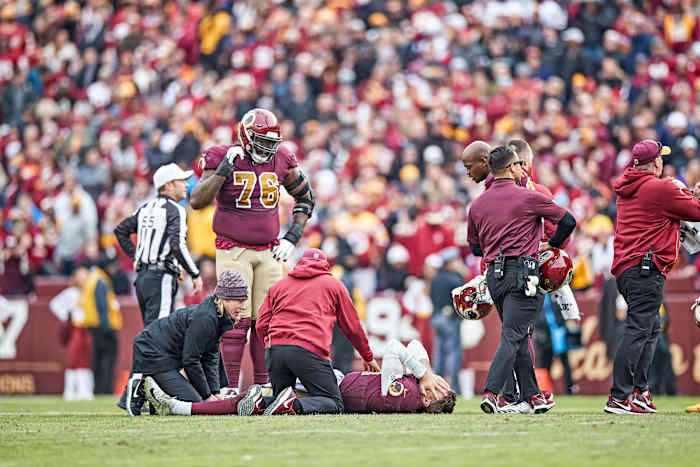 Alex Smith lies on the field with his hands over his face after breaking his right leg during a 2018 game